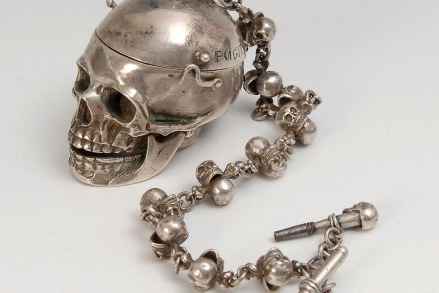 Außergewöhnliche silberne Spindeluhr als Memento Mori. 19. Jh. Undeutlich gepunzt, Gewicht (mit Kette und Schlüssel) 267 g. Gehäuse in Form eines Totenschädels, mit beweglichem Unterkiefer und aufklappbarer Schädeldecke, graviert "Fugit Irreparable Tempus"