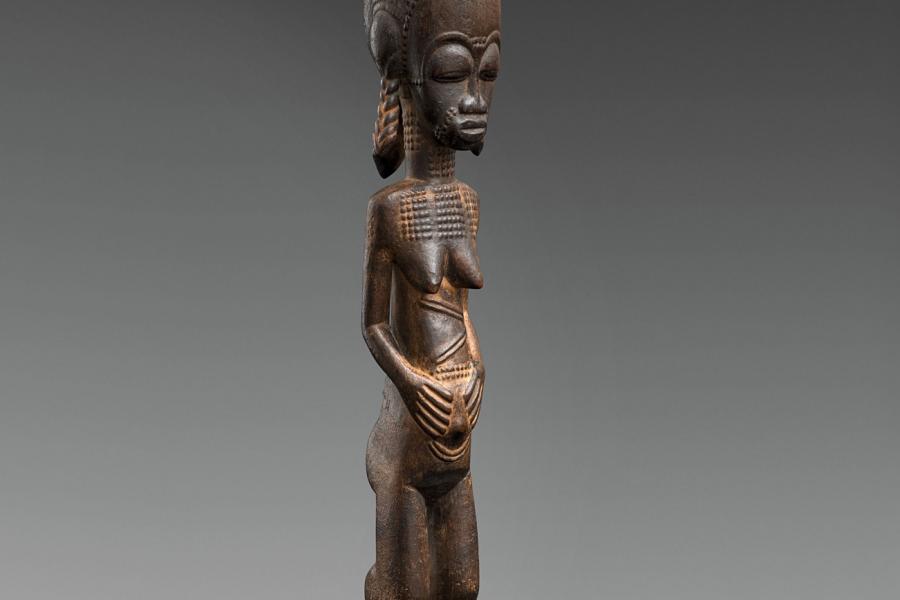 A BAULE FIGURE  Ivory Coast  The standing female with hands on the abdomen, the coiffure with tall top knot and three plaits, keloids on face, neck and body, on circular base, dark glossy patina.  43 cm. high Provenienz  Christie’s London, 7 July 1982, lot 19.  Schätzpreis: €15.000 - €20.000, Ergebnis: 40.000