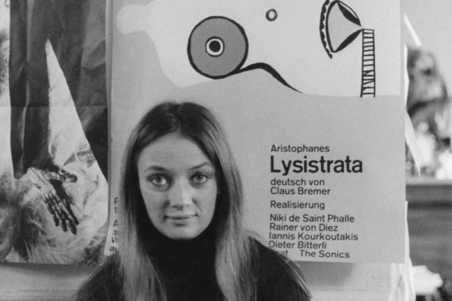 Niki de Saint Phalle vor dem Plakat zu Lysistrata sitzend, 1966 © Foto: unbekannt © 2016 Niki Charitable Art Foundation, All rights reserved.