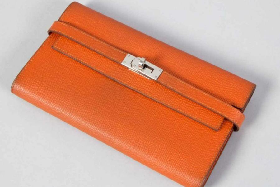 Hermès-Portemonnaie "Kelly" Orangefarbenes Ziegenleder. Rechteckige Form mit Klappdeckel und Drehverschluss. Silberfarbene Beschläge. Reißverschlusstasche und mehrere Kartenfächer im Inneren. 20 x 11,5 cm. Gebrauchssp. Orig.-Hermès-Rechnung von 2019 über eine professionelle Reinigung und Hermès-Beutel vorhanden.  Aufrufpreis:	450 EUR